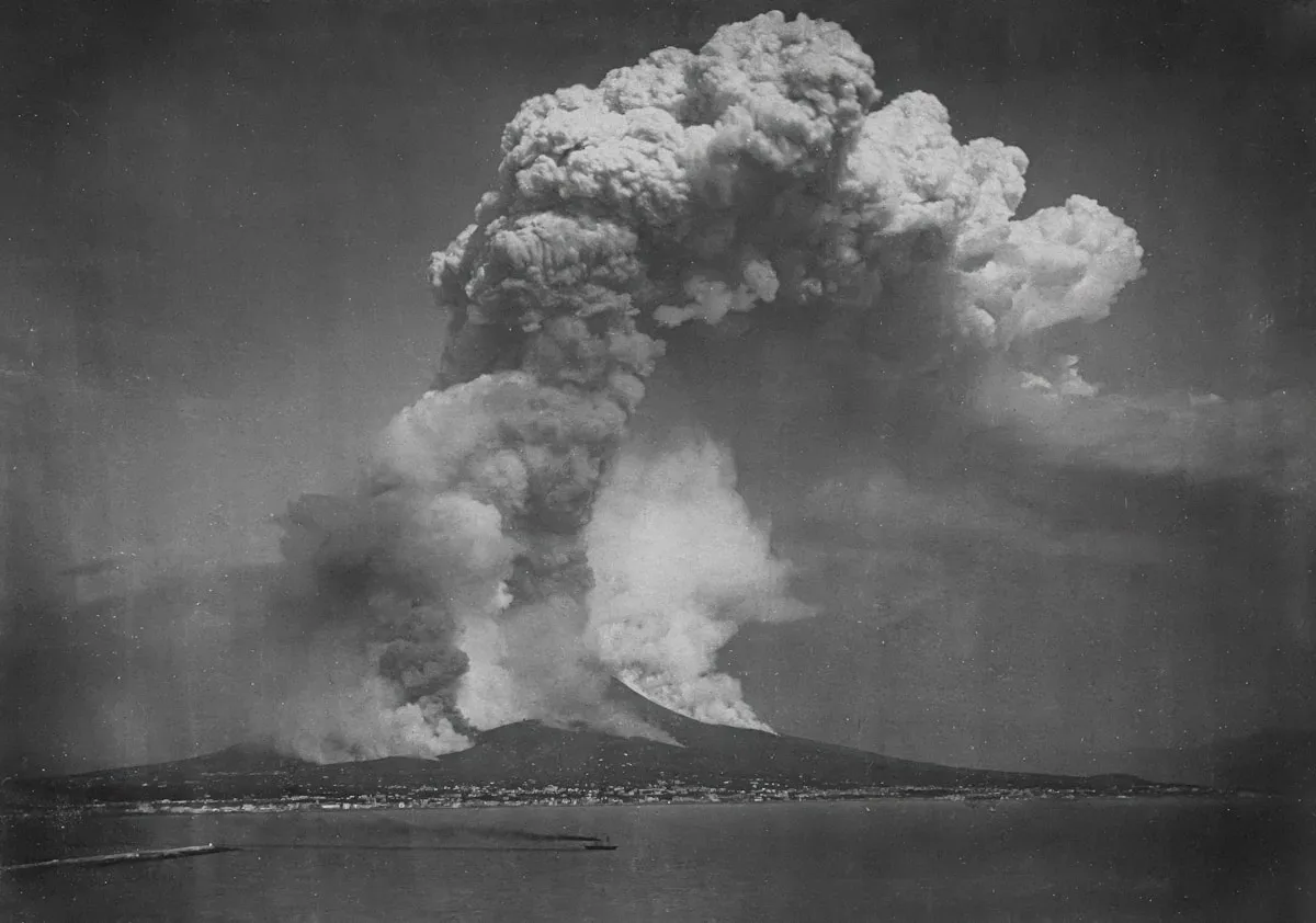 Volcano erupting with a large ash cloud over town.